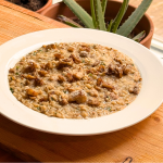 Bord romige risotto met oesterzwammen, gegarneerd met gebakken paddenstoelen en geraspte kaas, geserveerd op een houten tafel bij het raam met planten op de achtergrond