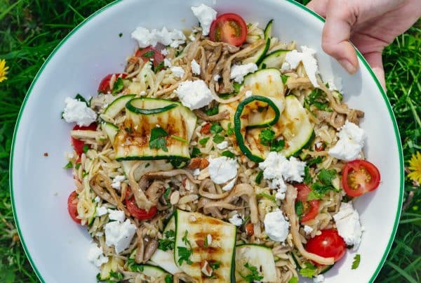 Ingrediënten voor orzo salade: oesterzwammen, courgette, cherrytomaatjes, feta, peterselie, citroen en kruiden op een aanrecht