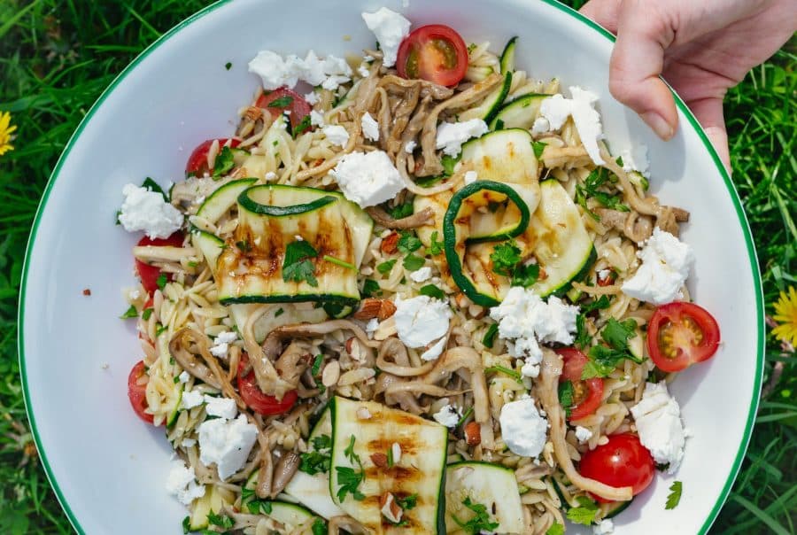 Ingrediënten voor orzo salade: oesterzwammen, courgette, cherrytomaatjes, feta, peterselie, citroen en kruiden op een aanrecht